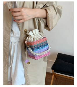 Detail of colorful woven bucket bag featuring pearl handle and gold chain strap