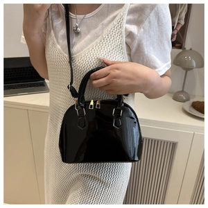 Detail of glossy black shell bag with gold hardware and dual zippers on a knit dress