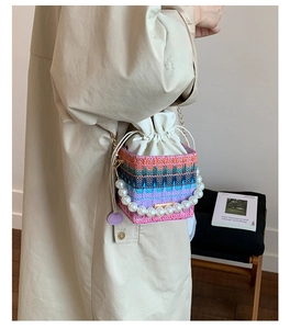 Detail of colorful woven bucket bag with pearl handle and metal chain on a model