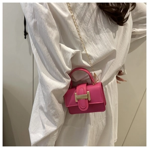 Mini magenta crossbody bag with gold chain strap and square metal buckle on white outfit