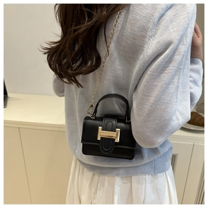 Close-up of black mini crossbody bag with golden H buckle worn by a model in dress