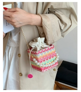 Detail of colorful woven bucket bag with oversized pearl handle and gold chain strap