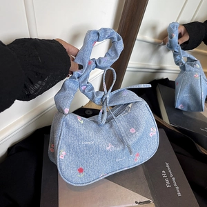 Floral denim shoulder bag with ruched handle and mirror reflection on book display