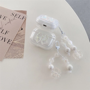 Macro detail of clear iridescent AirPods case with pearl bow charm on beige desk