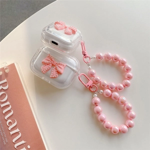 Clear AirPods case with pink bow and beaded bracelet strap on a white desk
