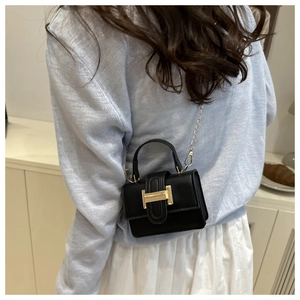 Detail of a mini black crossbody bag featuring a gold H-shaped buckle and chain strap