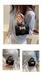 Detail of a mini black leather crossbody bag with a gold belt buckle and metal chain strap