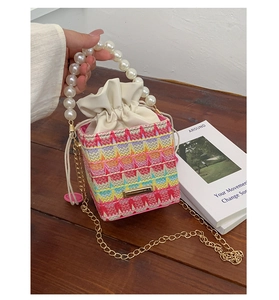 Detail of colorful woven bucket bag with large pearl handle and golden chain strap