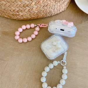 Detail of AirPods cases with pink bows, white stars, and pearl bead lanyards on wooden table
