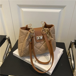 Quilted beige tote bag with brown leather trim and golden metal lock on a white book