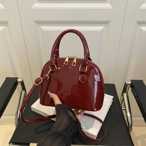 Glossy burgundy shell-shaped patent leather handbag with gold zippers and crossbody strap