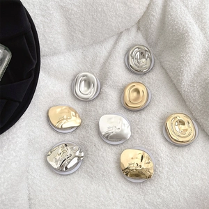 Flat lay of geometric metallic phone griptoks in gold and silver on soft white fabric