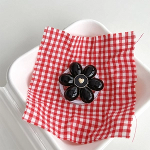 Detail view of a black flower phone socket with a gold heart on a red checkered cloth