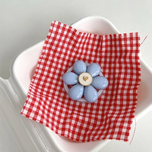 Detail view of light blue flower phone grip with golden heart on red checkered cloth
