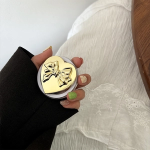 Close-up of golden heart-shaped phone grip with relief bow on hand with lace sleeves