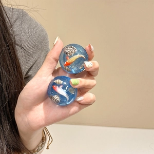 Blue resin sphere phone grip with miniature goldfish and shell, held by hand