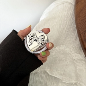 Detail of a heart-shaped silver phone grip featuring a 3D metallic bow and shiny finish