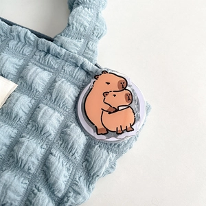 Gedetailleerd zicht op een schattige capibara acryl telefoonhouder op een blauwe tas