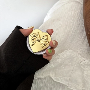 Close-up of heart-shaped phone grip with golden finish and bow detail held in hand