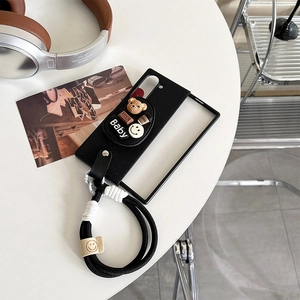 Détail d'une coque en cuir noir avec breloques 3D et cordon de transport tissé