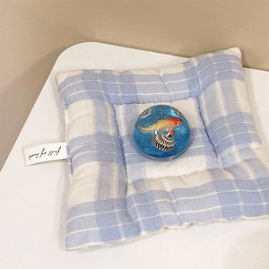 Close-up of blue goldfish resin ball holder on a blue checkered knit pad with luck label