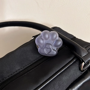 Detail of a purple jelly cat paw phone grip with a heart relief on a black nylon bag