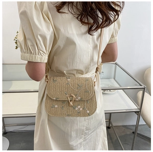 Detail of floral embroidery on a straw saddle bag with a golden metal clasp