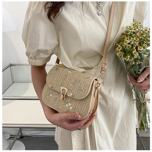 Straw saddle bag detail with floral embroidery and vintage gold metal lock closure