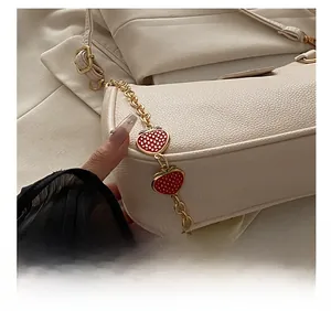 Close-up of white pebble leather bag featuring gold chain with enamel strawberry charms