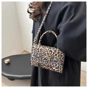 Detail of leopard print crossbody bag with gold bow buckle worn on person