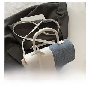 Detail show of two-tone crossbody bag with white leather handle and blue denim texture flap