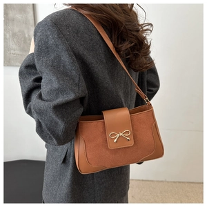 Detail view of brown suede crossbody bag with gold bow clasp on grey blazer suit