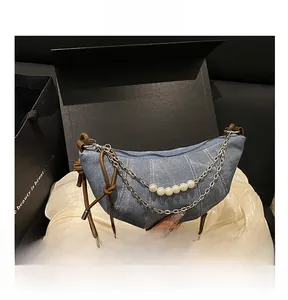 Dettaglio borsa a mezzaluna in denim blu con catena di perle e tracolla annodata