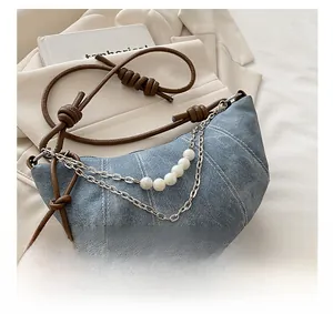 Dettaglio borsa a mezzaluna in denim con fili di perle, catene e tracolla in pelle annodata