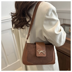 Detail of a brown suede and leather shoulder bag with a gold bow buckle on a model