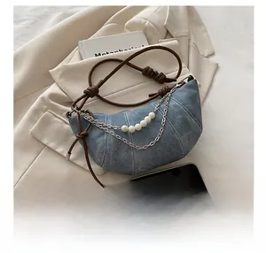 Dettaglio borsa a mezzaluna in denim con catena di perle e tracolla in pelle marrone annodata