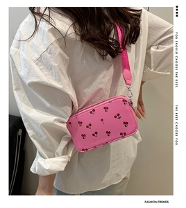 Close-up of pink crossbody bag featuring cherry patterns and wide shoulder strap detail
