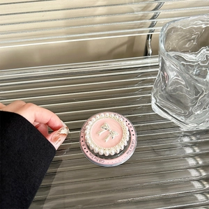 Close-up of pink phone grip featuring a silver bow and pearl trim on a metal tray