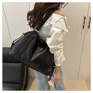 Side view of large black leather tote bag with wide shoulder strap on model in minimalist room