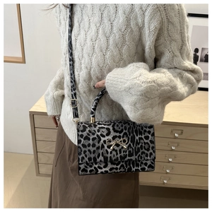 Close-up of a small leopard print handbag with golden bow metal clasp worn by a model
