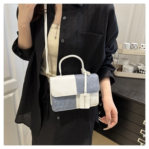 Detail view of stylish white leather and blue denim patchwork handbag with strap