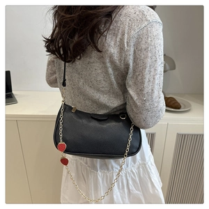 Detail of black lychee grain leather bag with decorative strawberry chain strap pendants
