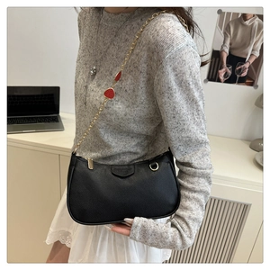 Detail of black litchi grain leather bag featuring a strawberry charm gold chain strap