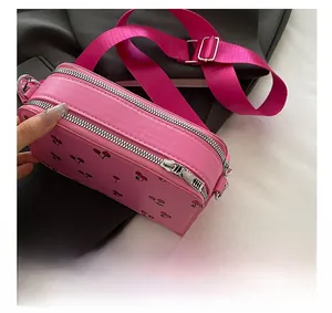 Detail view of pink leather crossbody bag showing dual zippers and red cherry print