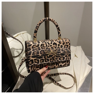 Detail of leopard print handbag featuring a gold bow buckle and adjustable shoulder strap