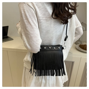 Détail du sac bandoulière noir avec franges et clous argentés dans un décor de café