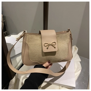 Close-up of beige shoulder bag featuring a golden bow buckle and mixed texture fabric