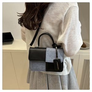 Detail of color-block crossbody bag featuring mixed textures and fashion tag accessory