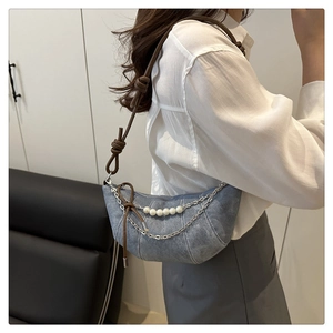 Detail view of denim croissant bag with pearl chain strap and brown knotted leather handle