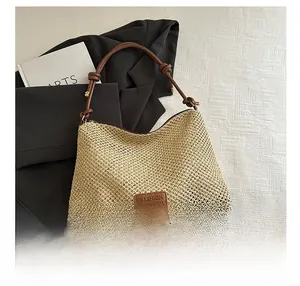 Detail of woven straw tote bag featuring brown leather handle and gold buckle accents